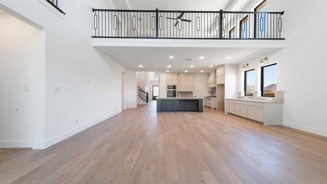 Unfurnished living room with a towering ceiling, stairs, light wood-style flooring, a ceiling fan, and recessed lighting