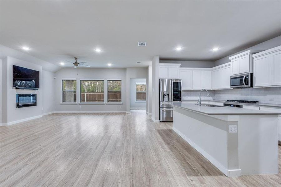 Kitchen with white cabinetry, stainless steel appliances, a glass covered fireplace, light wood finished floors, and a ceiling fan Kitchen with white cabinetry, stainless steel appliances, a glass covered fireplace, light wood finished floors, and a ceiling fan