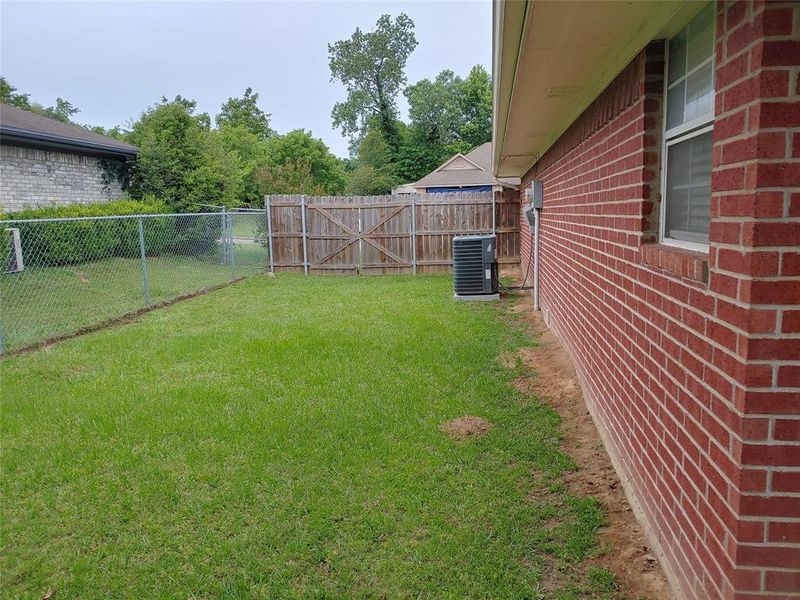 Expansive green space featuring chain link and wood fencing, a red brick exterior, and an air conditioning unit