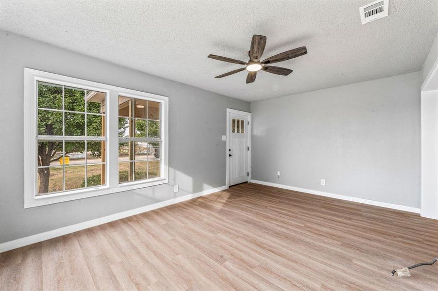 Empty room featuring light wood finished floors, a textured ceiling, and a ceiling fan Empty room featuring light wood finished floors, a textured ceiling, and a ceiling fan