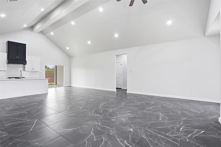 Open-concept living area with vaulted ceilings, recessed lighting, and large format dark tile flooring
