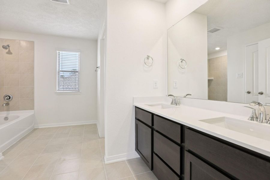 This additional view of the primary bath highlights an oversized tub/shower combination with tile surround, and a large window with blinds that offers both natural light and privacy.
