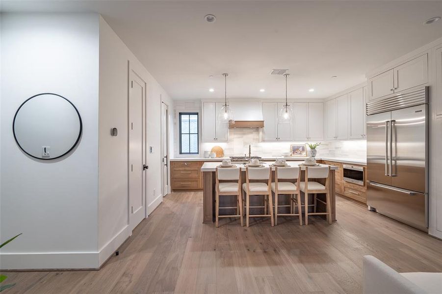 Kitchen with an island with sink, white cabinets, decorative backsplash, hanging light fixtures, and built in appliances