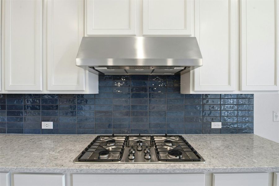 Kitchen with exhaust hood, stainless steel gas stovetop, white cabinetry, and light stone countertops