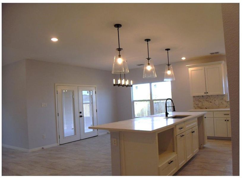 Kitchen with sink, an island with sink, pendant lighting, and white cabinets