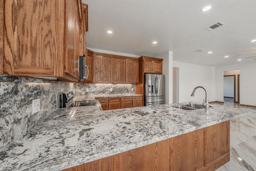 Kitchen featuring light stone counters, visible vents, appliances with stainless steel finishes, brown cabinetry, and a sink