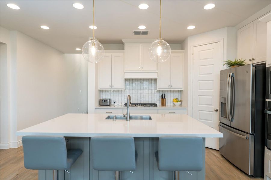 Kitchen featuring white cabinetry, stainless steel appliances, hanging light fixtures, a kitchen island with sink, and backsplash