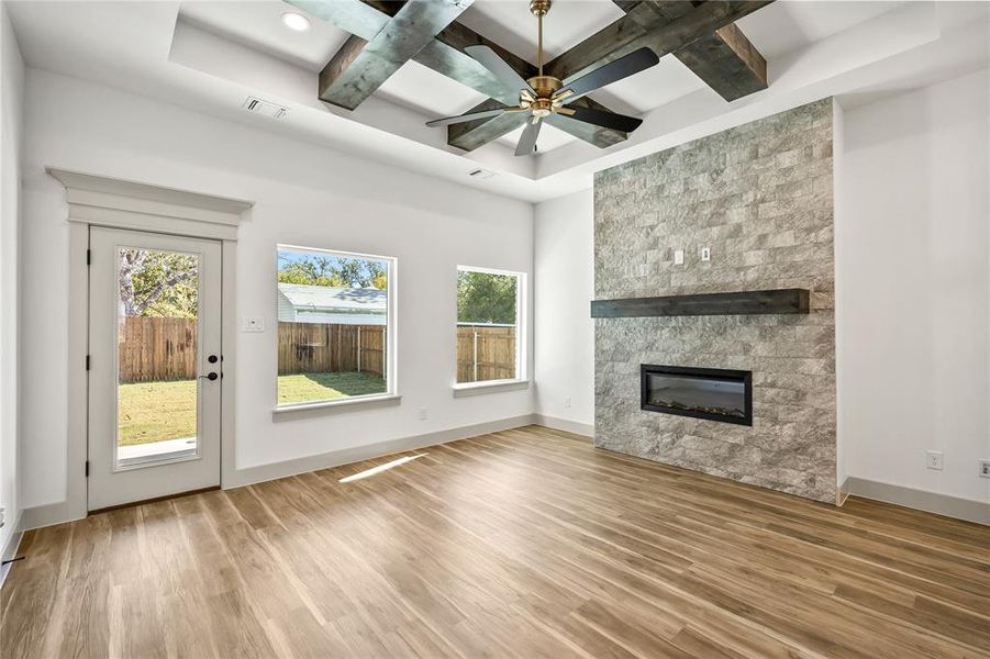 Unfurnished living room with coffered ceiling, beam ceiling, a fireplace, a ceiling fan, and light wood finished floors