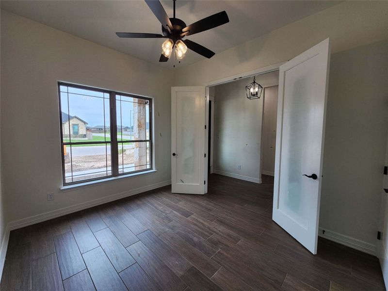 Spacious room featuring wood-finish tile flooring, a large window with grid pattern, and a ceiling fan with integrated lighting