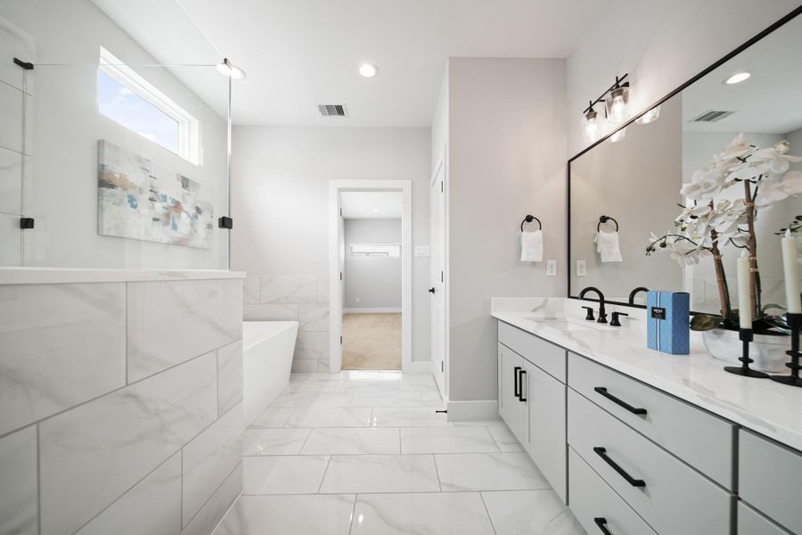 The dual sinks sit beneath quartz counters and are complemented by black plumbing fixtures and black cabinet hardware with a framed mirror and lights above. A private water closet provides added convenience, complete with built-in cabinets for extra storage. The dual sinks sit beneath quartz counters and are complemented by black plumbing fixtures and black cabinet hardware with a framed mirror and lights above. A private water closet provides added convenience, complete with built-in cabinets for extra storage.