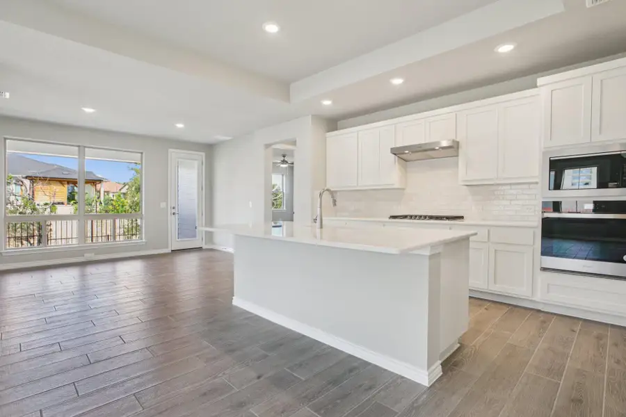 Kitchen featuring recessed lighting, stainless steel oven, white cabinets, backsplash, and a center island with sink