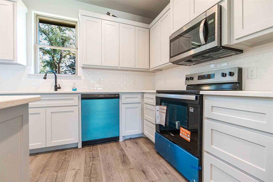 Kitchen with appliances with stainless steel finishes, backsplash, light wood-style flooring, and white cabinets