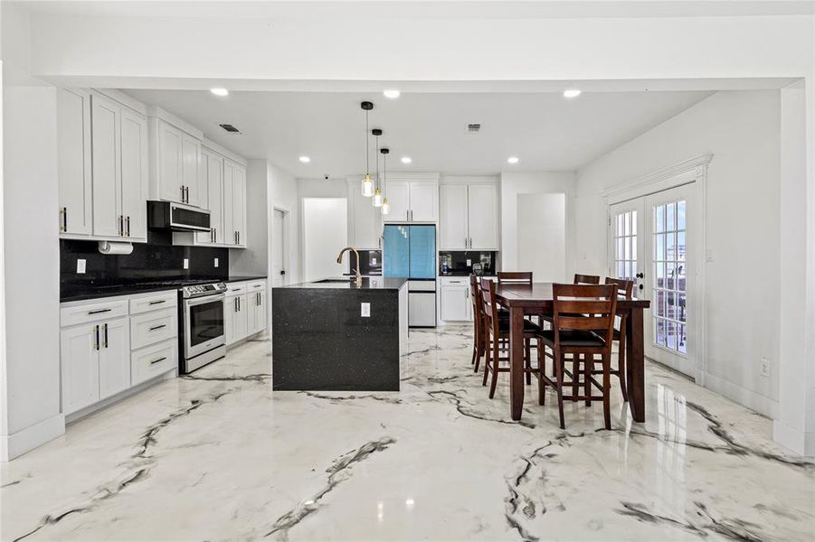 Kitchen featuring tasteful backsplash, an island with sink, hanging light fixtures, white cabinets, and recessed lighting Kitchen featuring tasteful backsplash, an island with sink, hanging light fixtures, white cabinets, and recessed lighting