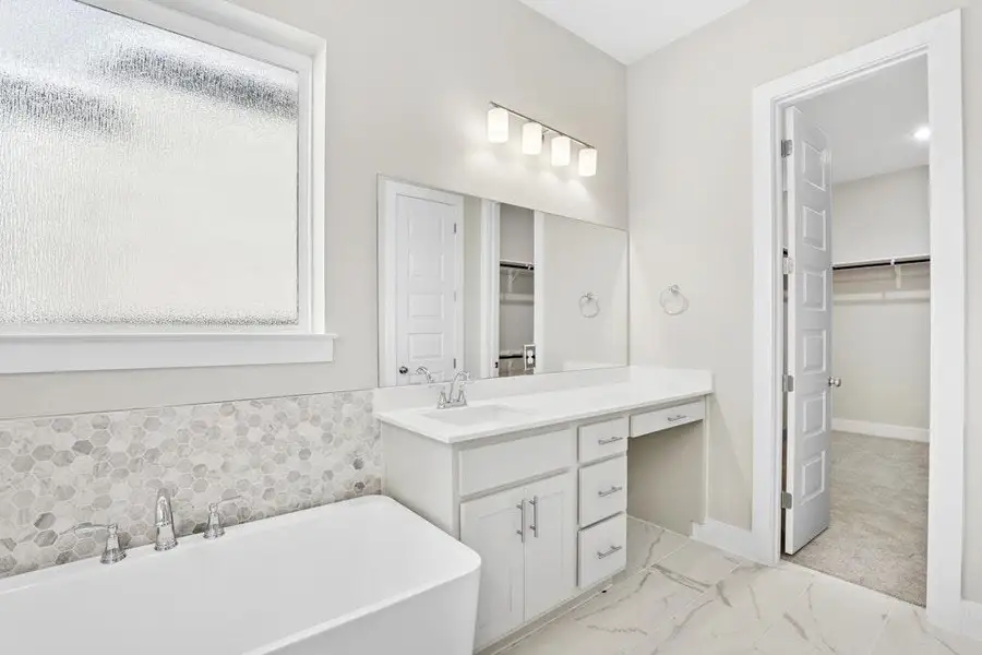 Full bathroom featuring a walk in closet, a freestanding bath, vanity, and light marble finish flooring Full bathroom featuring a walk in closet, a freestanding bath, vanity, and light marble finish flooring