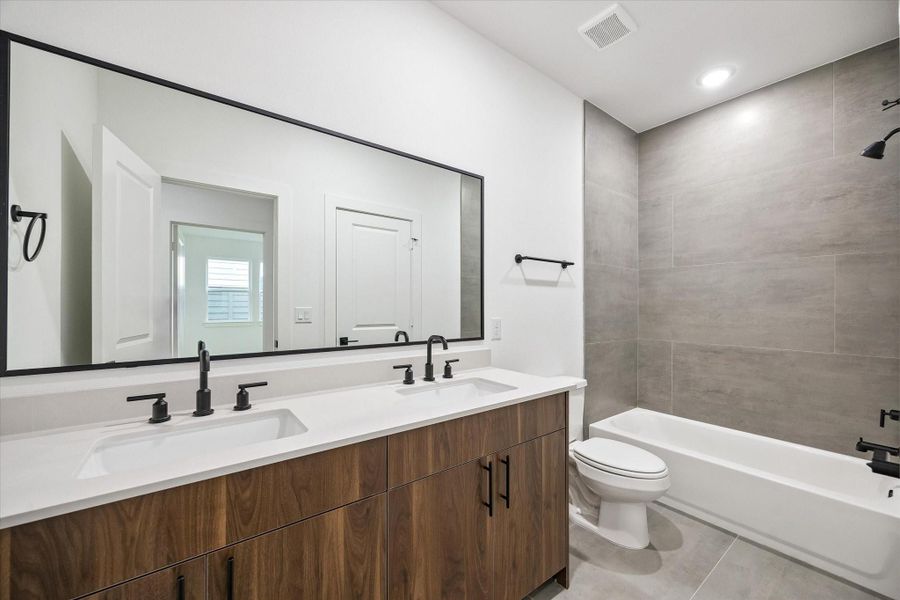 Full bath with dual vanity, large mirror, and sleek tile surround
