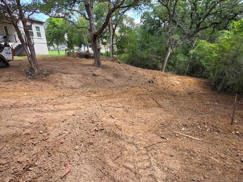A spacious, cleared lot with mature trees, ready for new construction, bordered by lush natural landscaping. A spacious, cleared lot with mature trees, ready for new construction, bordered by lush natural landscaping.