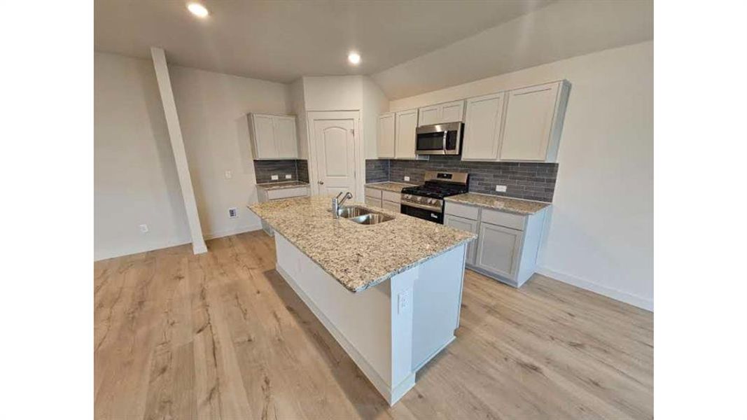 Contemporary kitchen featuring an island with a double basin sink, light-toned cabinetry, stainless steel appliances, a subway tile backsplash, and light wood-finish flooring