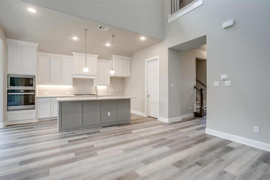 Kitchen featuring light wood-type flooring, stainless steel oven, black microwave, and a center island with sink