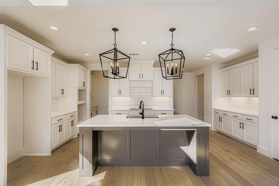 Kitchen featuring white cabinets, a center island with sink, decorative light fixtures, light wood finished floors, and recessed lighting