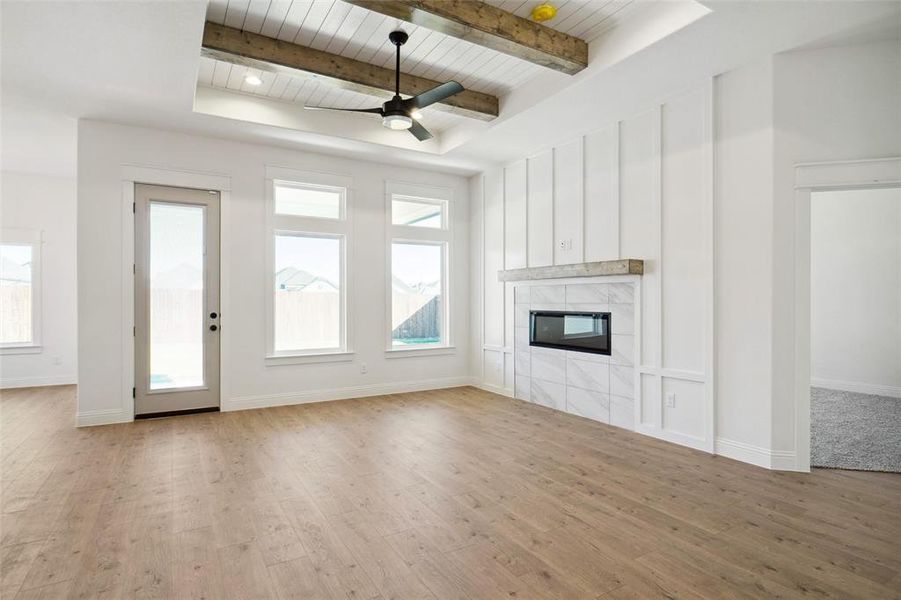 Unfurnished living room with beam ceiling, a tiled fireplace, wooden ceiling, and light hardwood / wood-style floors