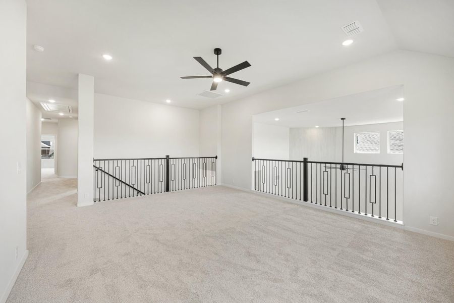 Open upstairs loft with carpet flooring, black metal railing, and ceiling fan with light fixture