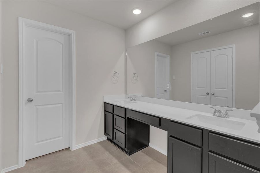 This primary restroom is a spacious, modern bathroom featuring a long vanity with dual sinks, ample under-sink storage, and a large mirror. The room has neutral color tones and is well-lit with recessed lighting.