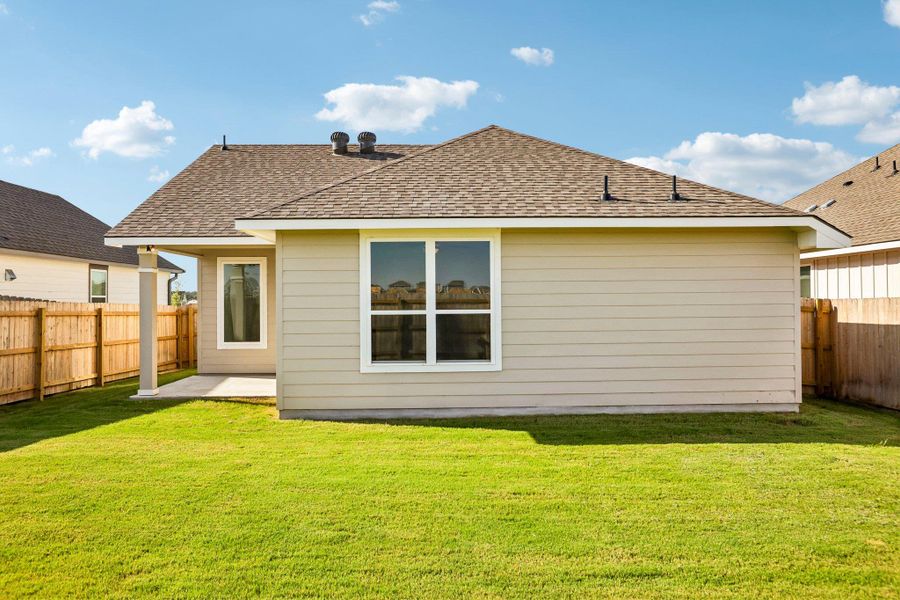 A flat grassy yard borders the rear exterior of this single-story residential home.