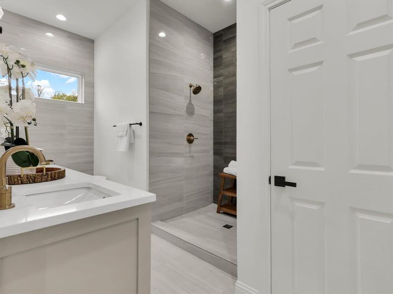 Bathroom with a tile shower, tile patterned flooring, and vanity