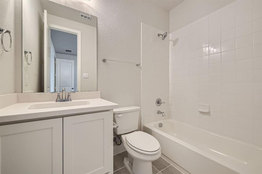 Full bathroom with tiled shower / bath combo, vanity, toilet, and tile patterned floors