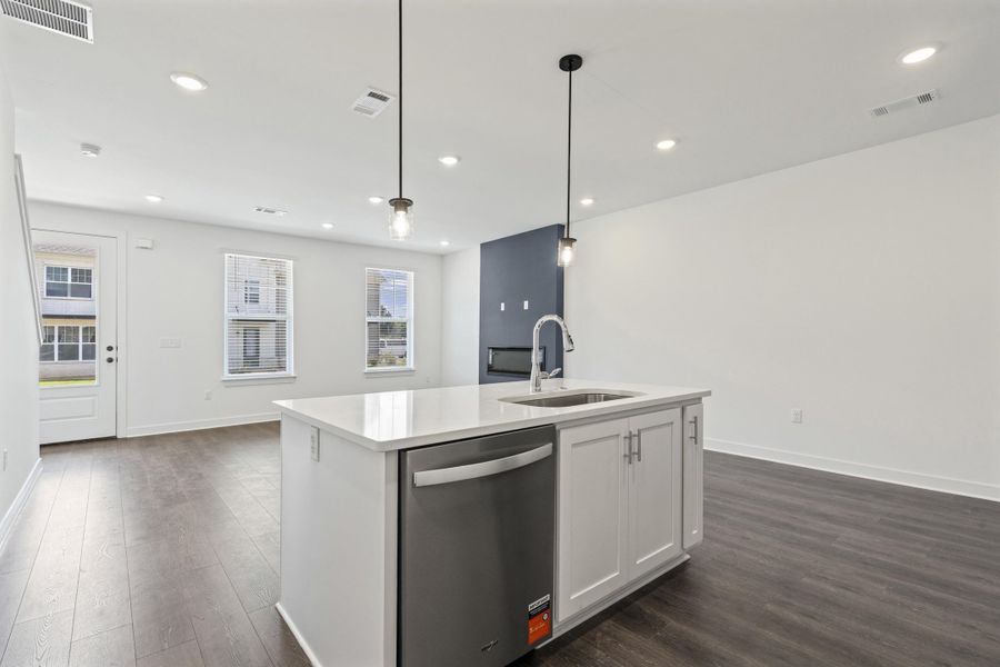 Open-concept living space with dark wood-finish flooring, recessed lighting, and a kitchen island featuring white cabinetry, a stainless steel dishwasher, and a sink with a gooseneck faucet