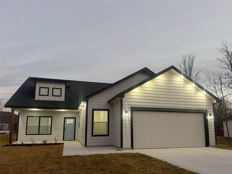 View of front facade featuring driveway, a garage, a shingled roof, and a front lawn