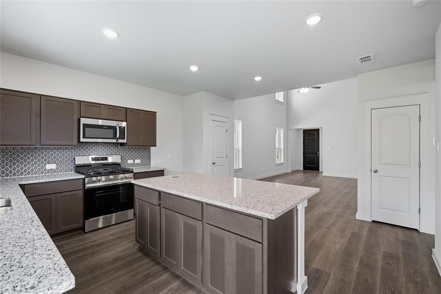 Kitchen with stainless steel appliances, dark brown cabinetry, light stone countertops, backsplash, and dark wood-style flooring Kitchen with stainless steel appliances, dark brown cabinetry, light stone countertops, backsplash, and dark wood-style flooring