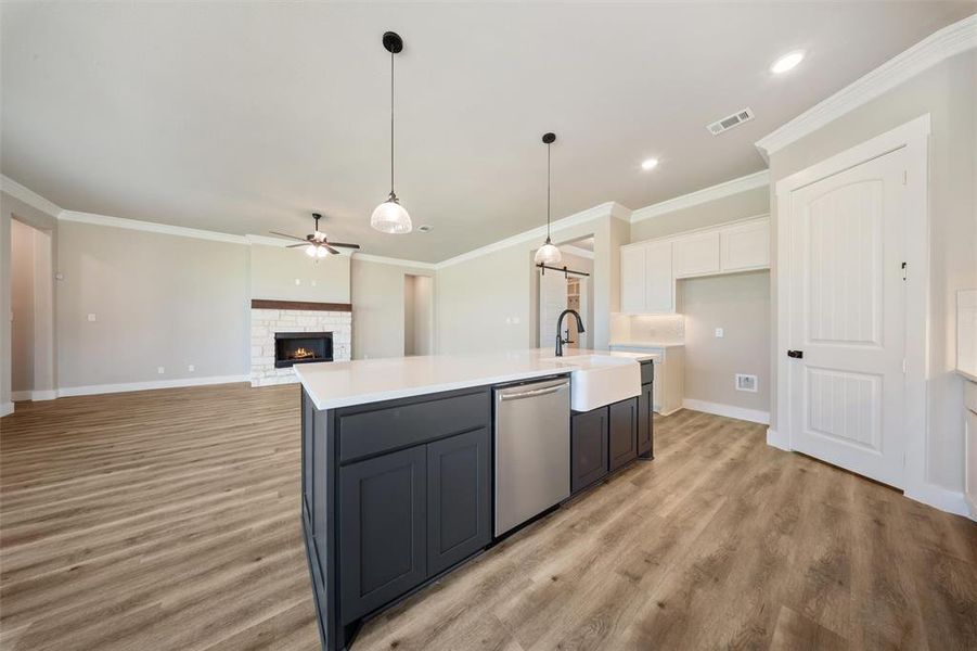 Kitchen featuring ceiling fan, light countertops, a stone fireplace, light wood-type flooring, and dishwasher Kitchen featuring ceiling fan, light countertops, a stone fireplace, light wood-type flooring, and dishwasher