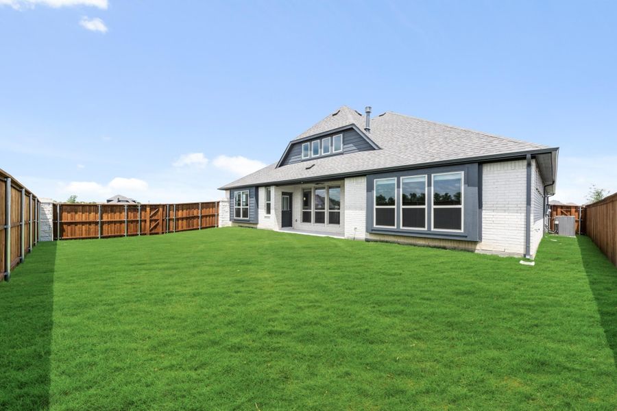 Backyard of a brick home with large lawn, wood privacy fence, and multiple rear windows.