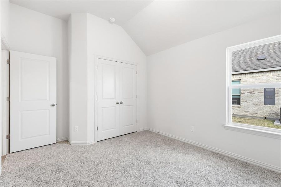 Unfurnished bedroom with light carpet, vaulted ceiling, and a closet Unfurnished bedroom with light carpet, vaulted ceiling, and a closet