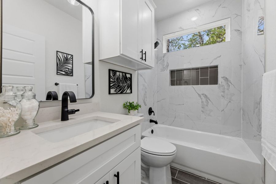 A well-appointed bath features crisp white cabinetry, a generous soaking tub, and striking marble-look tile work.