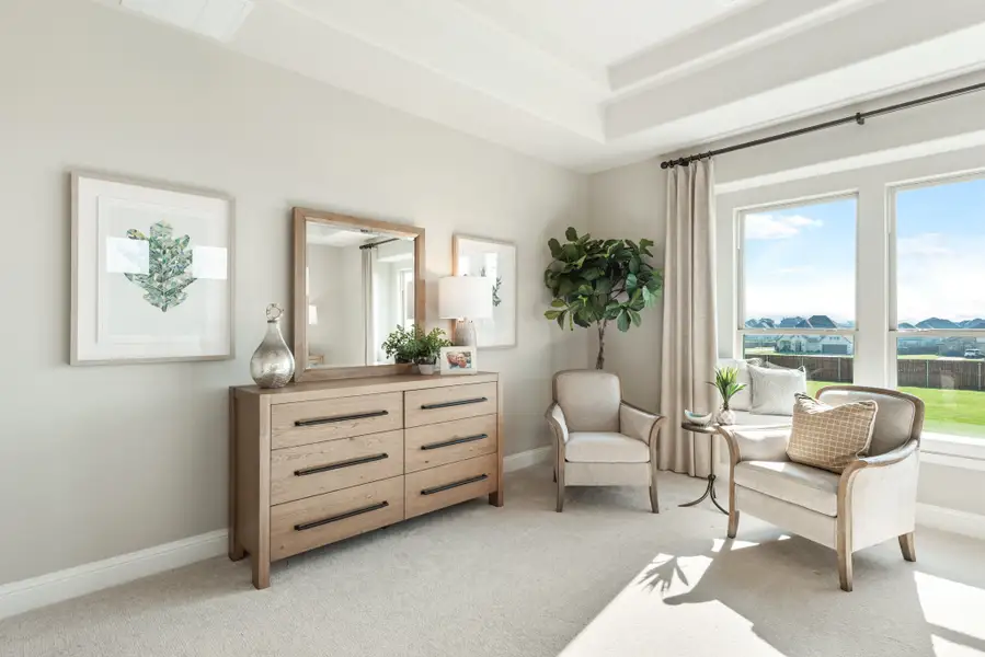 Bedroom sitting area with wood dresser, mirror, two accent chairs, and large windows with outdoor view