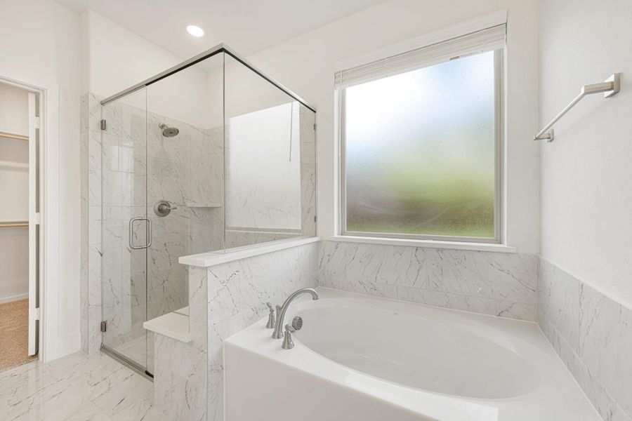 Master bathroom with soaking tub, glass-enclosed shower, and marble tile walls and floors