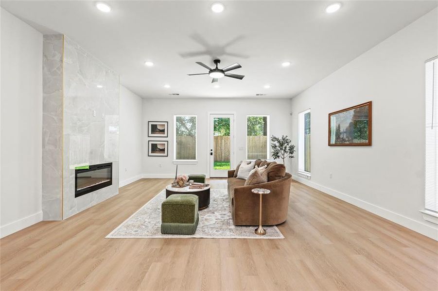 Living room with a fireplace, ceiling fan, light wood-style floors, and recessed lighting Living room with a fireplace, ceiling fan, light wood-style floors, and recessed lighting