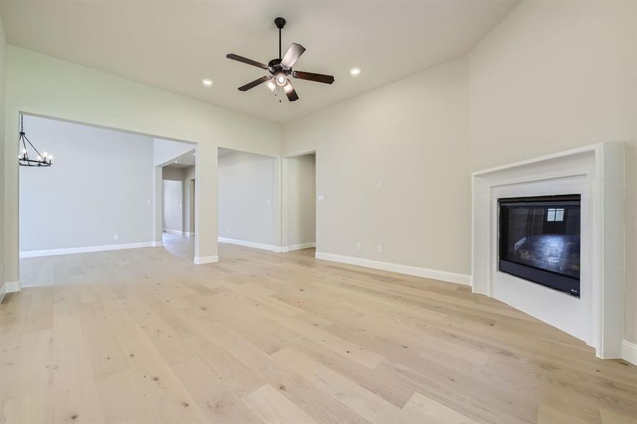 Unfurnished living room featuring ceiling fan with notable chandelier and light wood-type flooring