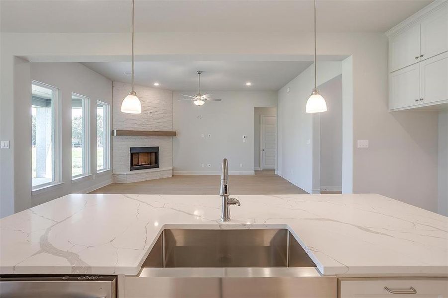 Kitchen with light wood-type flooring, a stone fireplace, white cabinets, light stone counters, and decorative light fixtures