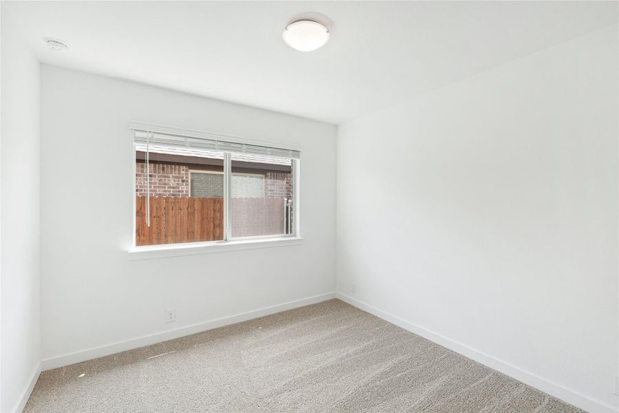Empty bedroom with white walls, beige carpet, and a single window with blinds