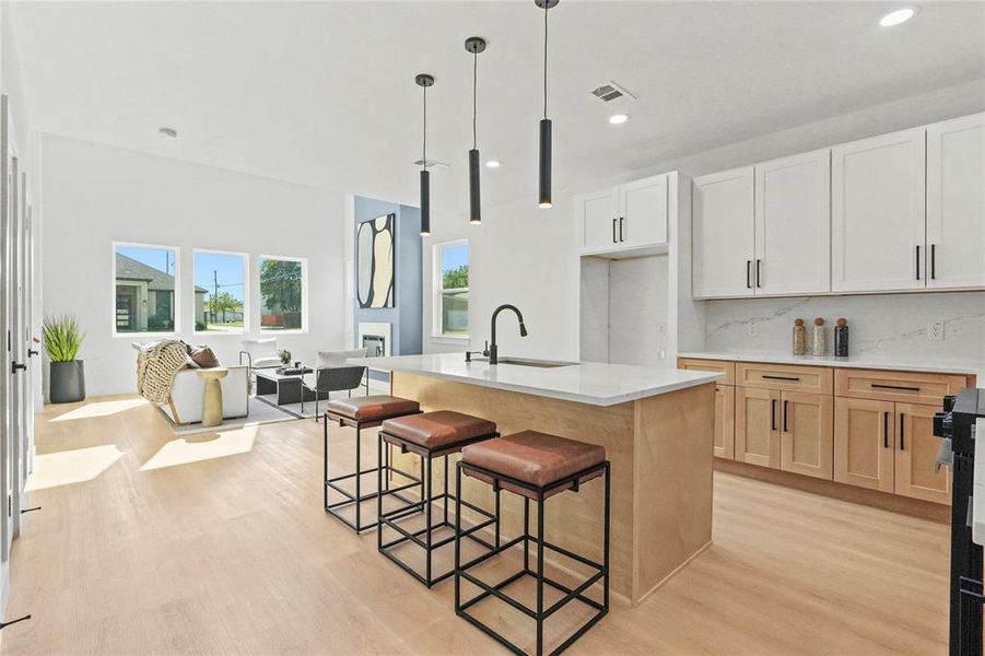 Kitchen featuring decorative light fixtures, a breakfast bar, tasteful backsplash, light wood-type flooring, and a center island with sink Kitchen featuring decorative light fixtures, a breakfast bar, tasteful backsplash, light wood-type flooring, and a center island with sink
