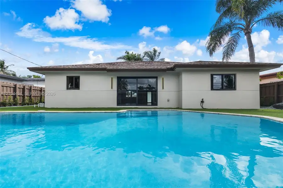 In-ground swimming pool, exterior sliding glass doors, horizontal wood privacy fencing, and neutral-toned stucco siding