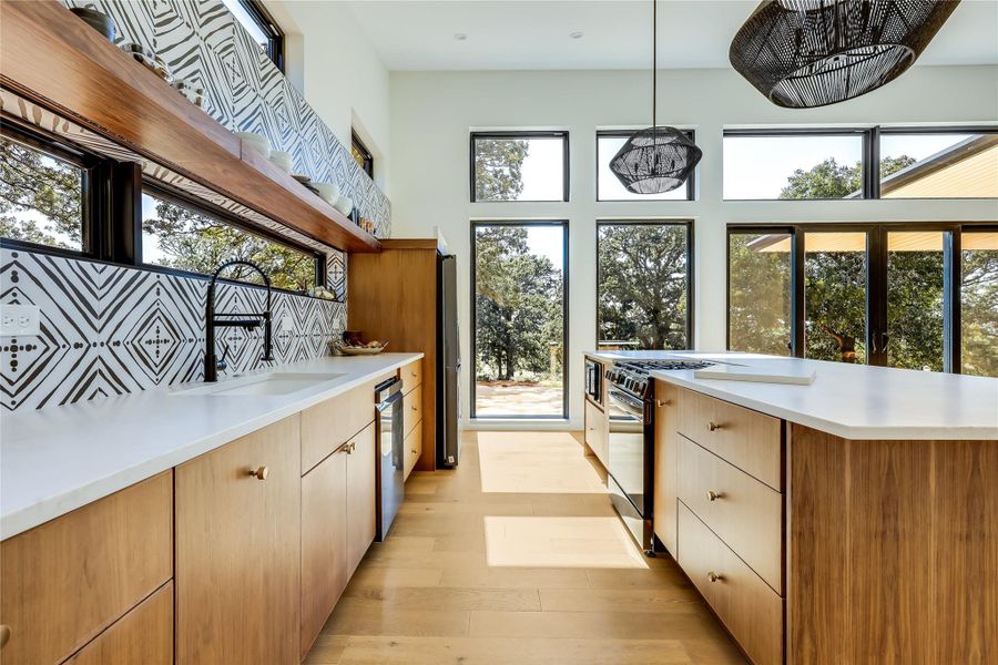Kitchen with pendant lighting, light wood-style flooring, light stone countertops, black gas range, and tasteful backsplash