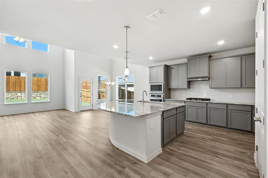 Kitchen with gray cabinets, appliances with stainless steel finishes, recessed lighting, light stone countertops, and wood finished floors Kitchen with gray cabinets, appliances with stainless steel finishes, recessed lighting, light stone countertops, and wood finished floors