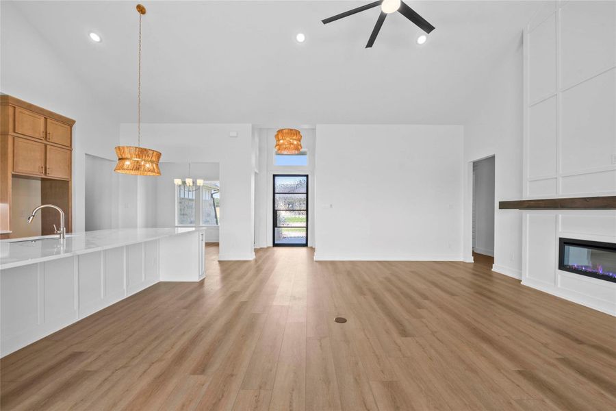 Unfurnished living room with vaulted ceilings, recessed lighting, luxury wood-look vinyl plank flooring, a glass covered fireplace, and an open concept kitchen Unfurnished living room with vaulted ceilings, recessed lighting, luxury wood-look vinyl plank flooring, a glass covered fireplace, and an open concept kitchen