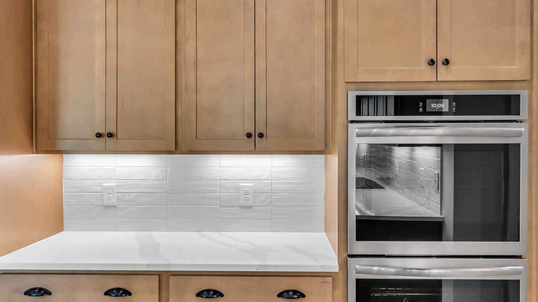 Kitchen with wood colored cabinetry and nearby gathering room (Representative of completed home)