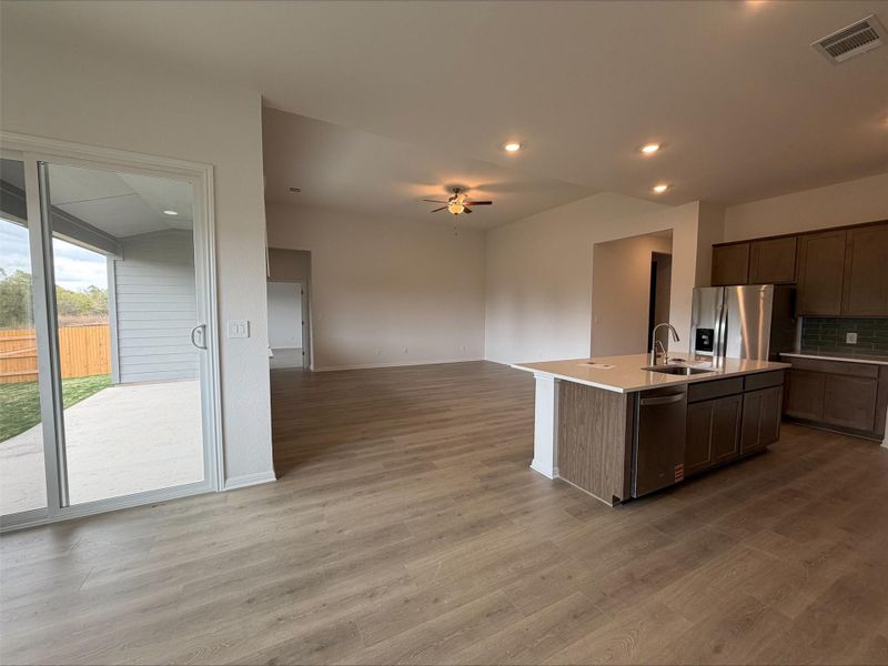 Kitchen with a kitchen island with sink, open floor plan, light wood-style floors, backsplash, and appliances with stainless steel finishes