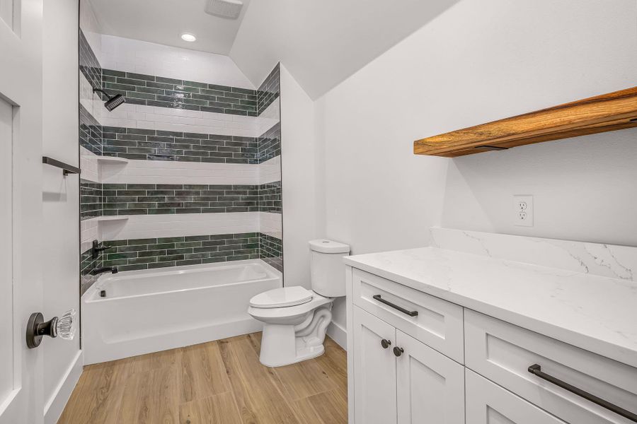 Full bath featuring toilet, lofted ceiling, wood finished floors, vanity, and washtub / shower combination